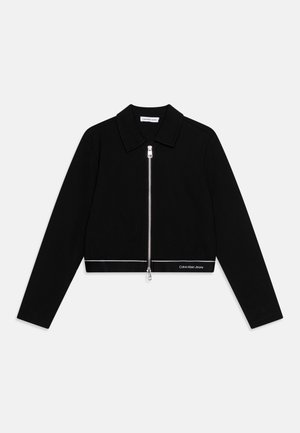 Schwarze, kurz geschnittene Jacke mit langen Ärmeln, silbernem Reißverschluss vorne, Kragen und weißem "Calvin Klein Jeans"-Logo nahe dem Saum auf der rechten Seite.