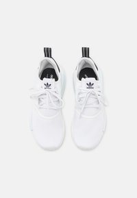 Vita sportskor i mesh-material med en svart och vit logotyp, vita snören och en texturerad sula. Svart accent på baksidan.