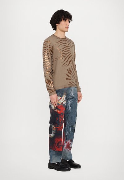 Beige long-sleeve shirt with metallic bronze zebra stripes; paired with blue jeans featuring a red floral design and distressed texture.