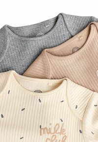 Drie geribbelde baby tops: grijs, beige en crème. De crème top heeft donkere zaadachtige accenten en geborduurde tekst "milk club". Zacht stof.