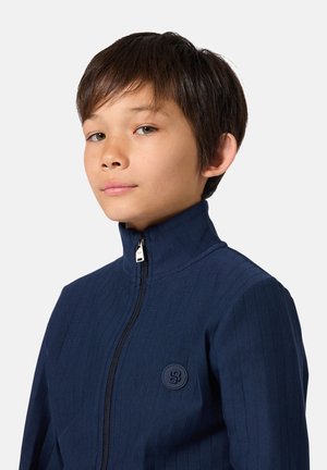 Veste zippée bleu marine avec texture côtelée, col montant et écusson rond sur la poitrine gauche. Tissu lisse avec une silhouette ajustée.