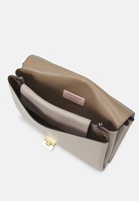 Beżowa i taupe'owa skórzana kopertówka z złotym zapięciem, otwarta, aby pokazać gładkie skórzane wnętrze i metkę marki z napisem "Coccinelle Autentyczna skóra włoska."