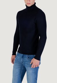 Maglione a collo alto a coste blu navy con un design aderente, maniche lunghe e una texture liscia, abbinato a jeans azzurri.