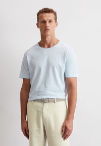 Helles blaues Baumwoll-T-Shirt mit kurzen Ärmeln und rundem Ausschnitt, kombiniert mit hellbeigen Leinenhosen und einem gewebten Gürtel.