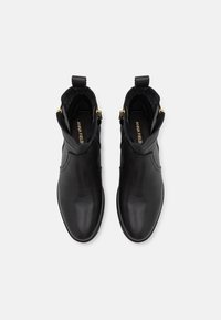 Bottines en cuir noir à finition lisse, avec des panneaux latéraux élastiques et des accents dorés, dotées d'un bout arrondi et de languettes pour un enfilage facile.