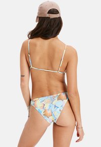 Bikini-set med ett fruktmönster i pastellfärger, justerbara axelband och en knytning i midjan. Materialet verkar slätt med minimal textur.