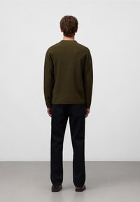 Olivgrünes Langarmoberteil mit strukturierter Oberfläche, kombiniert mit dunklen Hosen. Das Design ist einfach, ohne sichtbare Logos oder Muster.