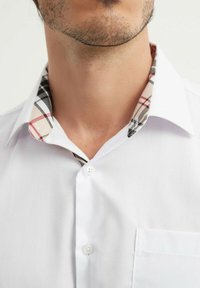Chemise blanche à boutons avec un col à motif à carreaux beige, noir et rouge. Texture lisse avec une poche poitrine du côté gauche.