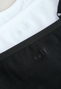 Close-up van geribd zwart-wit stof met het woord "soft." geborduurd op elk met bijpassende draad.