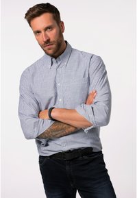 Camicia con bottoni a righe blu e bianche, maniche lunghe arrotolate ai polsi e taschino sul petto. Abbinata a jeans scuri.