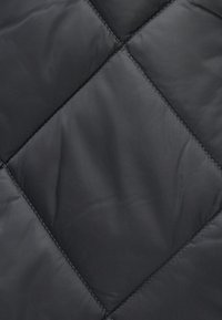 Tissu matelassé noir avec un motif en diamant, présentant une texture lisse et des accents de couture visibles. Le matériau semble brillant et léger.