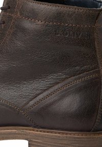 Bottine en cuir marron avec une surface texturée, des coutures contrastées et une semelle basse de style bois. Marquage discret sur le côté.