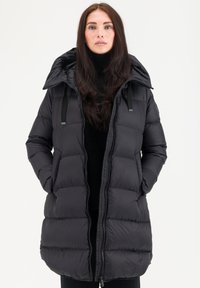 Veste en duvet noire avec capuche, présentant un design matelassé, deux poches avant et une fermeture éclair. Texture lisse et bretelles réglables.