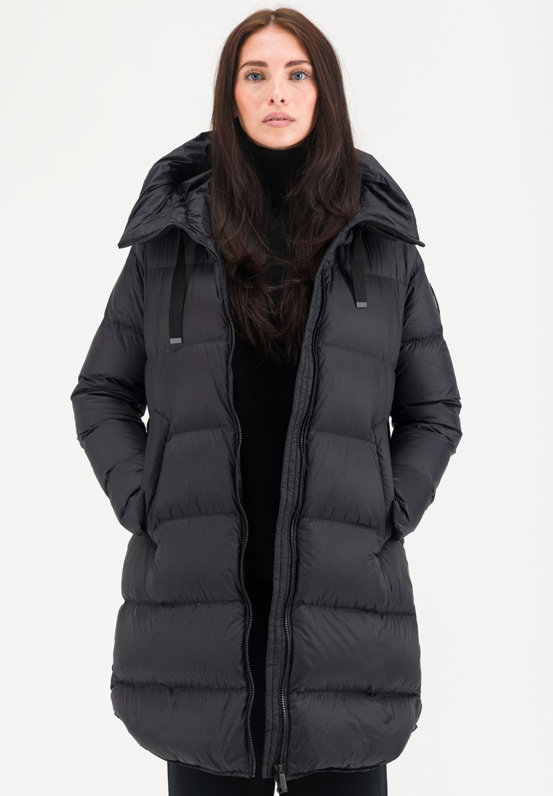 Veste en duvet noire avec capuche, présentant un design matelassé, deux poches avant et une fermeture éclair. Texture lisse et bretelles réglables.