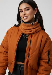 Orange puffer jacket with a quilted pattern, paired with a ribbed orange cowl neck. The model wears hoop earrings and a black top beneath.