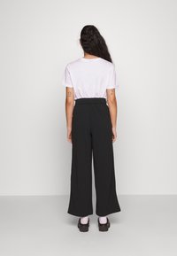 Svarta vidbyxor med hög elastisk midja, parat med en ljusrosa kortärmad t-shirt, sedd från baksidan.