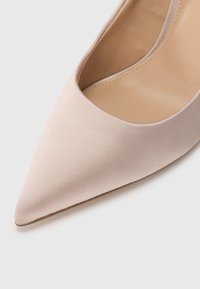 Γυμνό σατέν γοβάκι με ψηλό τακούνι, μυτερή μύτη, καμπυλωτές πλαϊνές εγκοπές και λεία εσωτερική επένδυση. Διαθέτει λεπτό, κομψό σχέδιο.