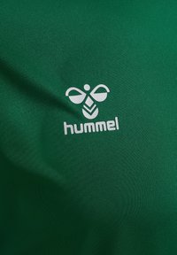 Grön sporttröja i mjukt tyg med en vit Hummel-logotyp och emblem på framsidan.