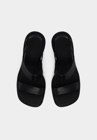 Μαύρα δερμάτινα σανδάλια με δύο φαρδιές λουρίδες, επίπεδες σόλες και ρυθμιζόμενες αγκράφες, φαίνονται από πάνω σε λευκό φόντο.