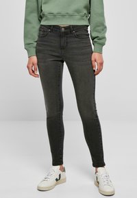 Jeans ajustados en denim gris oscuro, que cuentan con un diseño clásico de cinco bolsillos, detalles de costura y un cierre frontal con botón. Combinados con zapatillas blancas.