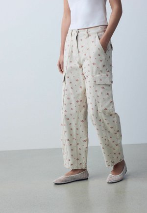 Woman wearing cream cargo pants with small pink floral print, paired with white mesh flats and a white sleeveless top.