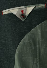 Dark green blazer with patterned inner lining showing repeated "GENTS CLUB" text and a triangular fabric detail with a button and red stitching.