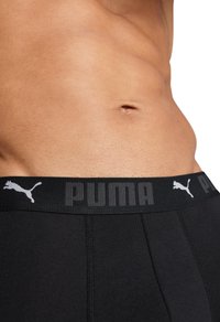 Fekete boxer alsónadrág széles rugalmas der�ékpánttal, amelyen szürke "PUMA" logó és egy puma sziluett található. Simás textúra, testhezálló forma.