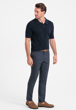Polo de manga corta en color navy con tejido texturizado, combinado con pantalones grises ajustados y mocasines de ante marrón, llevados con un cinturón marrón.