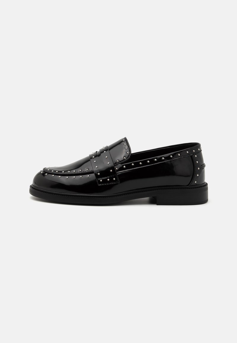 Musta patenttihihnainen loafer-mallinen kenkä, jossa on hopeanvärisiä metallinappeja yläosassa ja kantapäässä. Kengät ovat sileäpintaiset ja matala, lohkareinen korko tekee niistä mukavat jalassa.