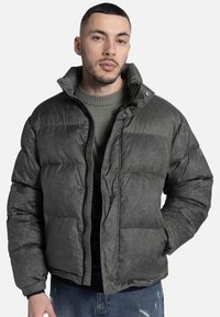 Sötétzöld, textúrált anyagból készült puffernadrág, magas gallérral, elülső cipzárral és patentgombokkal, vízszintes steppelt részekkel.