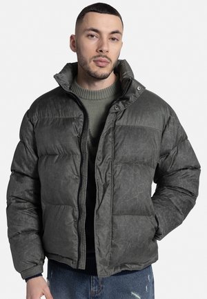 Bunda typu puffer vyrobená z tmavozelenej štruktúrovanej tkaniny s vysokým golierom, predným zipsom a patentkami, so sekciami horizontálneho prešívania.