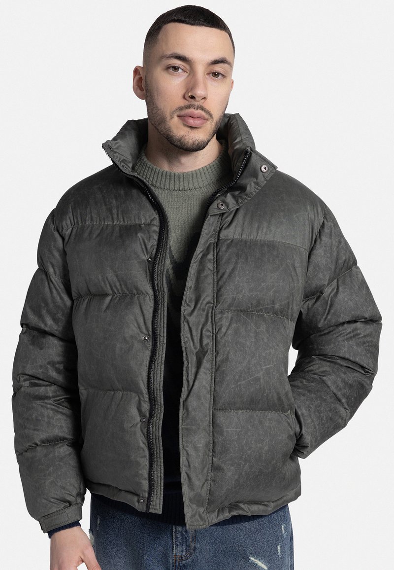 Sötétzöld, textúrált anyagból készült puffernadrág, magas gallérral, elülső cipzárral és patentgombokkal, vízszintes steppelt részekkel.