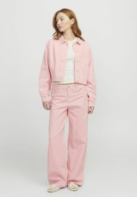 Svijetlo ružičasta skraćena kord jakna s džepom, uparena s odgovarajućim hlačama visokog struka širokih nogavica, obje s vertikalnim prugama.