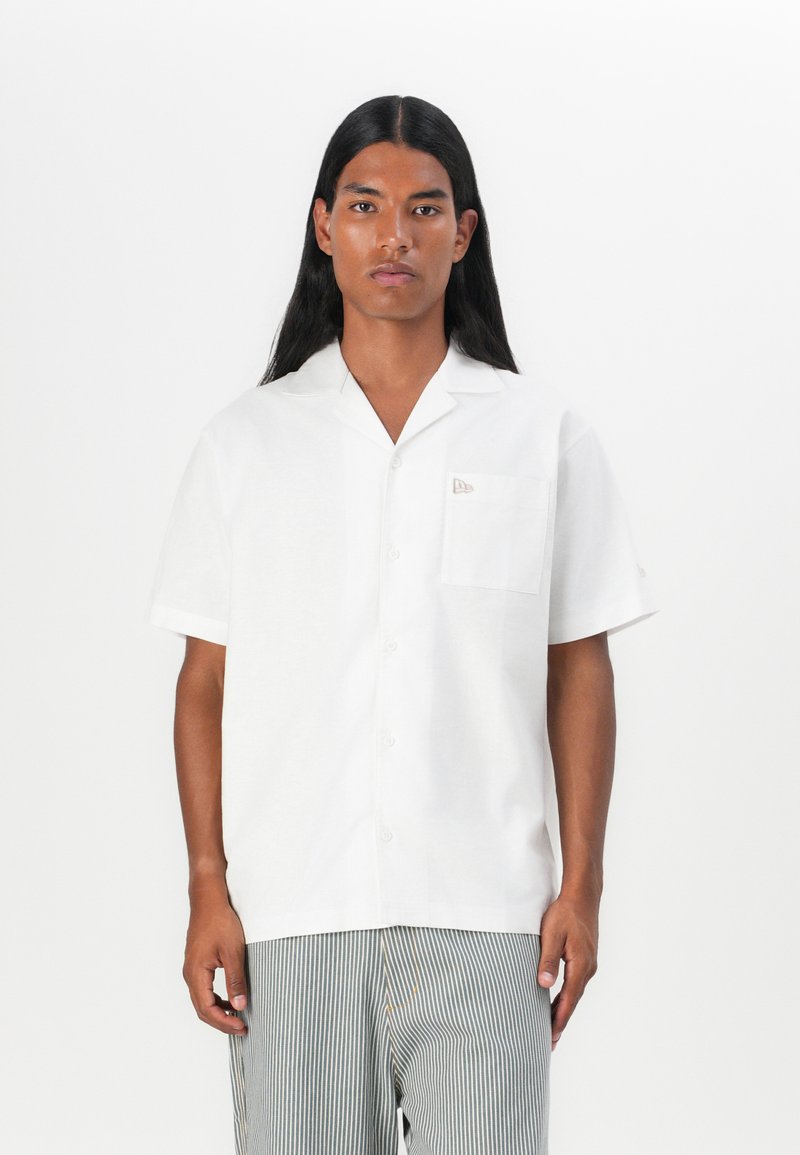 Camicia bianca a maniche corte in un materiale leggero, con taschino sul petto e un piccolo logo ricamato sulla tasca.