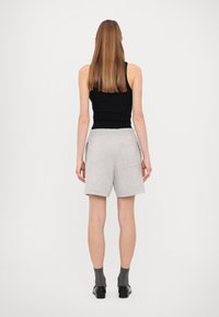 Pilkos medvilnės šortai su laisvu siluetu, su šoninėmis kišenėmis ir elastingu juosmeniu, derinami su prigludusia juoda marškinėliais be rankovių. Atvirkštinis vaizdas.