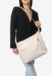 Borsa a tracolla in pelle beige chiaro con finitura texturizzata, dotata di una tasca frontale con zip e di una tracolla elegante.