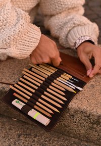 Boîte à crayons en bois avec des crayons de couleur assortis, un stylo gel blanc et une gomme, le tout maintenu par des élastiques sur une base en cuir brun.
