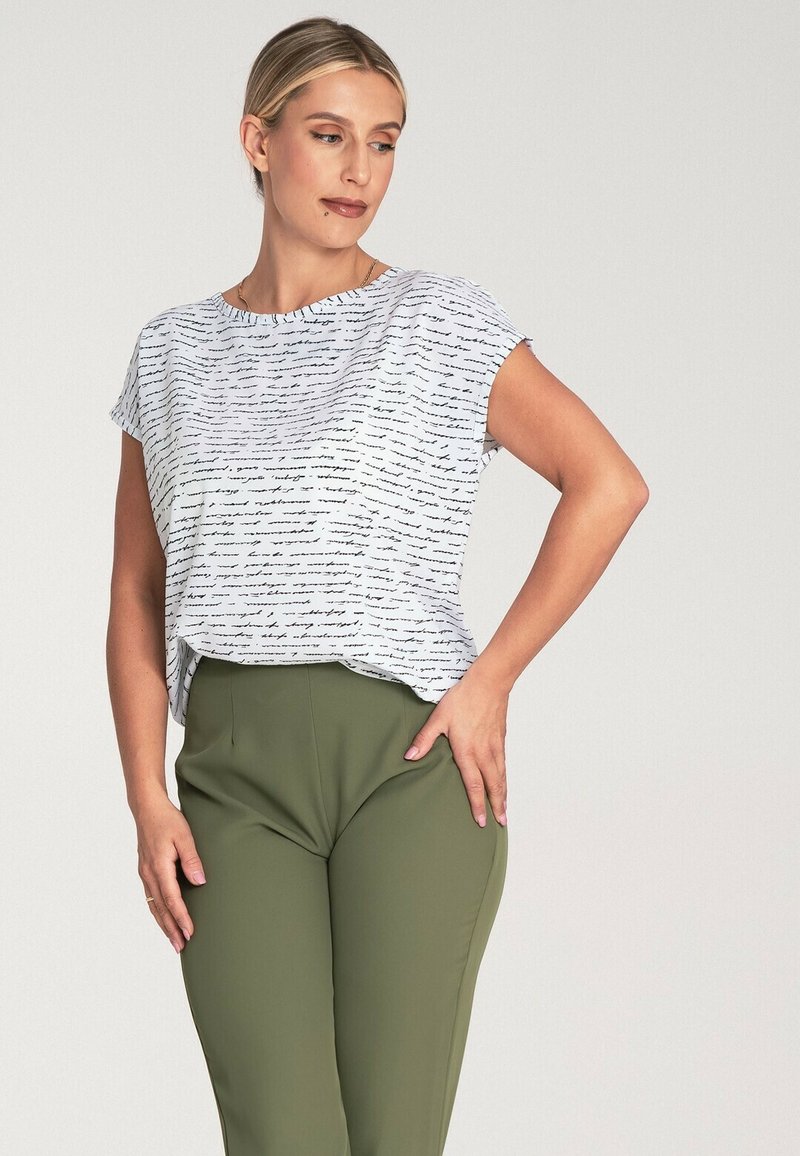 Biała bluzka krótki rękaw z odręcznym czarnym wzorem, zestawiona z oliwkowozielonymi spodniami o wysokim stanie. Gładki materiał z luźnym krojem.