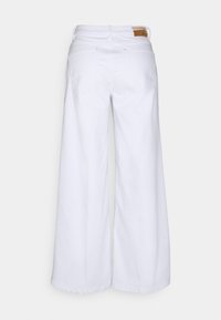 Jeans blancs à jambes larges en denim, avec une taille haute, deux poches arrière et une étiquette en cuir marron à la taille.