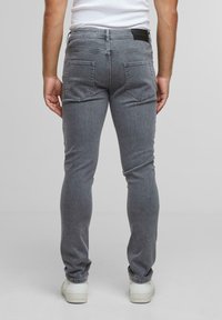 Harmaat slim-fit farkut, joissa on viisi taskua, ommeltuja yksityiskohtia ja nahkabrändilogo takavyötäröllä. Valkoiset tennarit täydentävät asustusta.