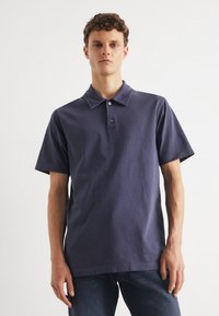 Granatowa koszulka polo z bawełny, z krótkim rękawem, z kołnierzykiem w szpic, z trzema guzikami oraz minimalnymi detalami w szwie. Casualowy krój.