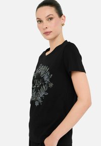 Sort bomulds t-shirt med korte ærmer, prydet med et blomster- og bogstavmotiv i sølv og klare udsmykninger. Glat tekstur.