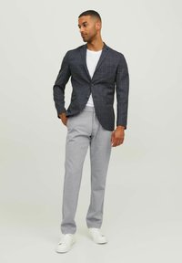 Marineblaues Karoblazer mit zwei Knöpfen und vorderen Taschen, kombiniert mit hellgrauen Hosen und weißen Sneakers auf einem neutralen Hintergrund.
