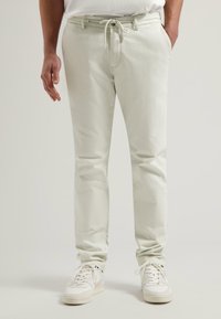 Pantalon slim clair avec une texture lisse, doté d'une taille à cordon de serrage et de poches latérales, associé à des baskets blanches.