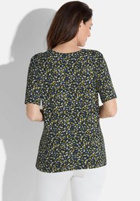 Kortemouwtop in een donkerblauwe stof met een veelkleurig gespikkeld patroon. Beschikt over een relaxte pasvorm en een ronde halslijn.