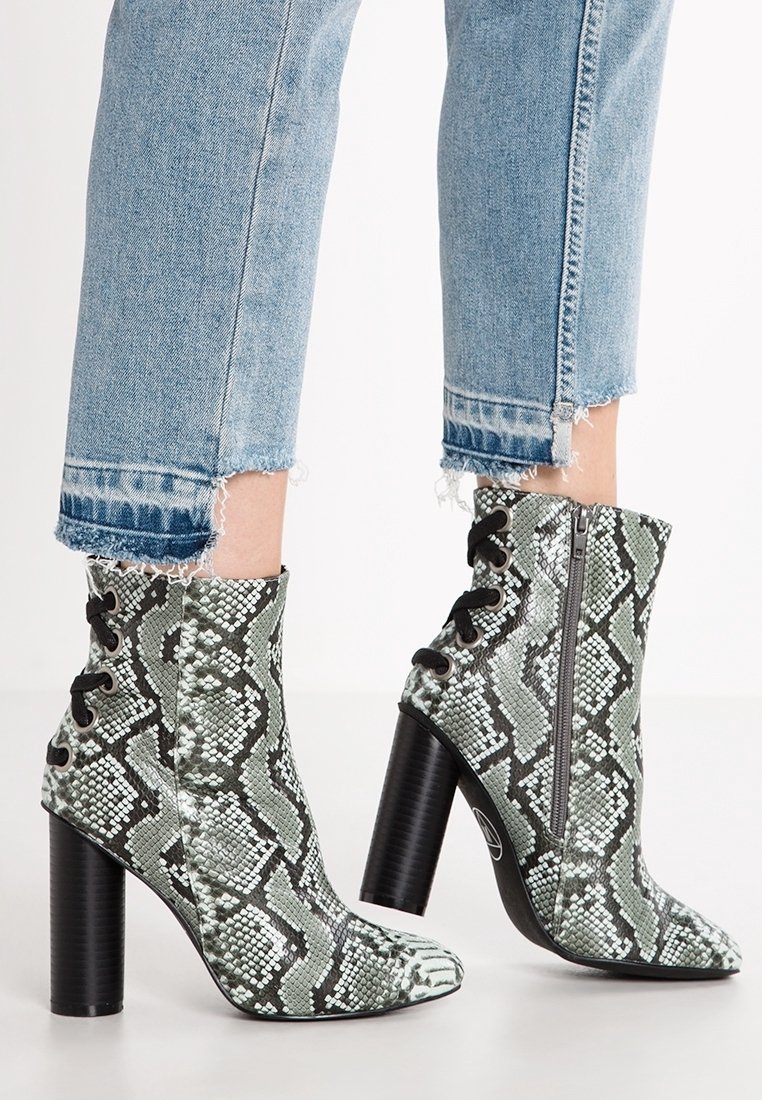 Bottines chevilles aux motifs serpent verts et noirs, avec un bout pointu, un talon bloc haut, des détails à lacets et une fermeture éclair sur le côté. Matériau synthétique texturé.