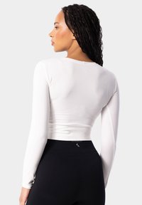 Balts garās piedurknes crop tops ar pieguļošu dizainu, gludu faktūru un apaļu kakla izgriezumu, apvienots ar melniem augstiem legingiem.