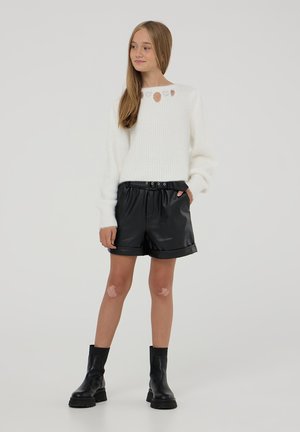 Maglione bianco lavorato a maglia con scollatura rotonda e fori decorativi, abbinato a pantaloni corte in finta pelle nera e stivaletti neri alla caviglia.
