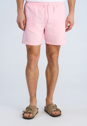 Man wearing light pink drawstring shorts and beige open-toe sandals, standing on a plain light background.
