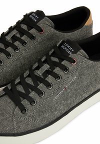 Gray canvas sneakers with black laces, featuring a white sole and subtle texture. The brand name is visible on the tongue and side.